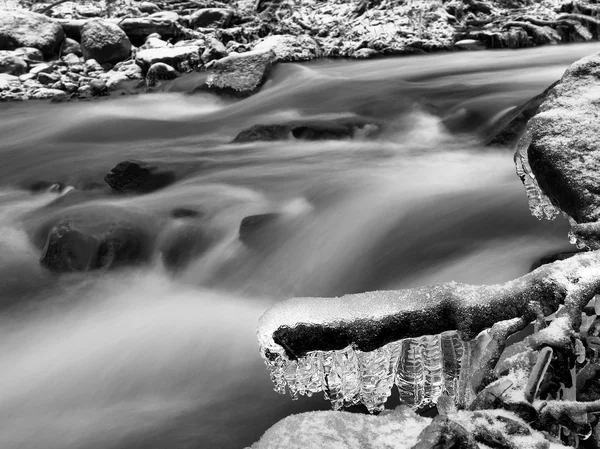 Vista nocturna de invierno a los carámbanos en ramitas y rocas heladas por encima de la corriente rápida. Reflejos de la lámpara de cabeza en carámbanos. Foto en blanco y negro . — Foto de Stock