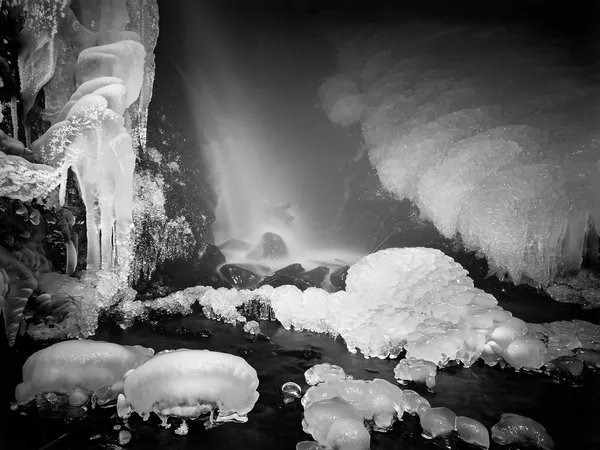 Nacht winter met het oog op bevroren cascade van waterval, ijzige twijgen en ijzige rotsen in bevroren schuim van snelle stroom. reflecties van licht in ijspegels. zwart-wit foto. extreme bevriezen. — Stockfoto