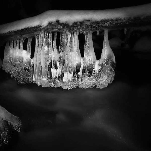 Vista nocturna de invierno a los carámbanos en ramitas y rocas heladas por encima de la corriente rápida. Reflejos de la lámpara de cabeza en carámbanos. Foto en blanco y negro . — Foto de Stock