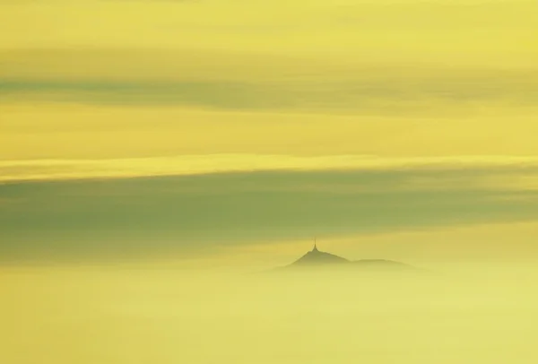 Misty daybreak in a beautiful hills. Peaks of hills are sticking out from foggy background, the fog is yellow and orange due to sun rays. — Stock Photo, Image