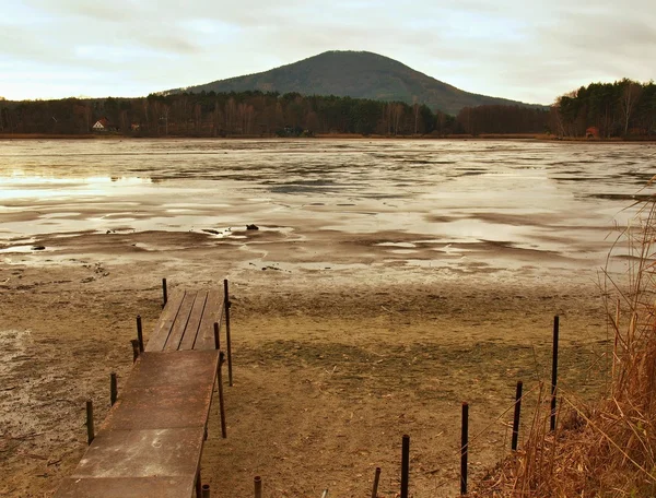 Verlassene alte hölzerne Maulwürfe am leeren Teich über schmutzigem Sand am Strand. Melancholische Herbststimmung. — Stockfoto