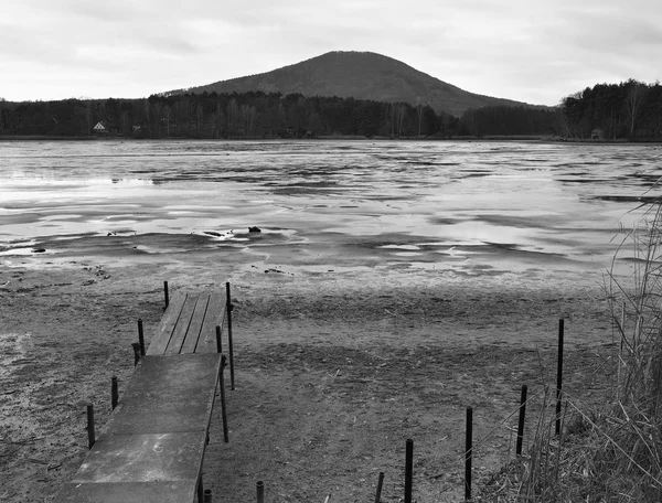 Abandoned old wooden mole at empty pond above dirty beach sand. Autumn melancholic atmosphere. — Stock Photo, Image