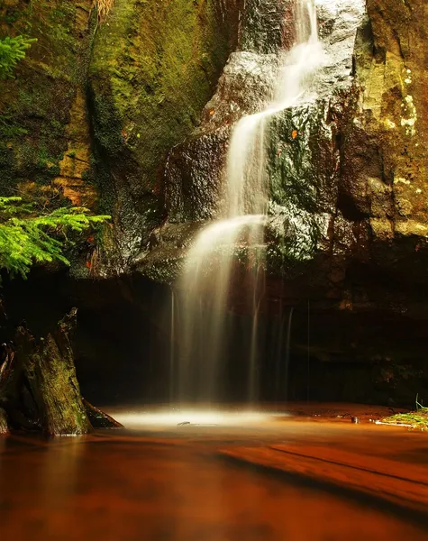 Cascata o piccola cascata sul ruscello di montagna fresca, l'acqua scorre sul blocco di arenaria muscolosa e salta giù in un piccolo torrente sottostante. Flussi d'acqua con raggi solari, sabbia arancione con sedimenti sottostanti . — Foto Stock