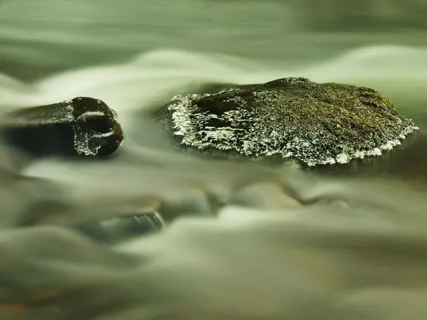 与小冰柱乳白色模糊水的山间溪流中的大石头。寒冷的冬天的天气 — 图库照片