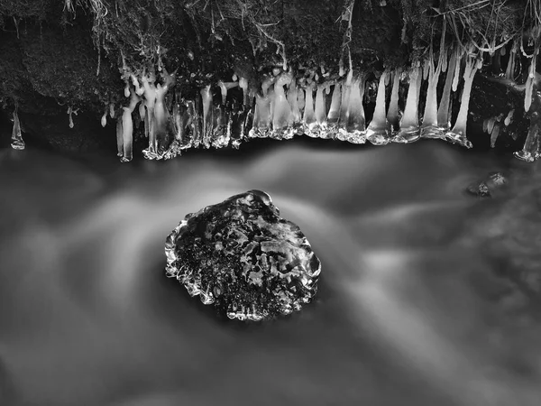 Congele a pedra de arenito musgosa na água fria escura do rio de montanha. Pequenos icicles brilham acima da água desfocada leitosa do córrego . — Fotografia de Stock