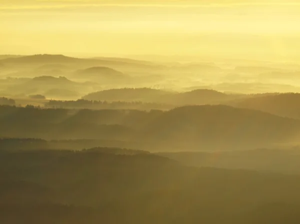 Herfst zonsopgang in een mooie berg van Bohemen. pieken van heuvels steeg van mistige achtergrond, de mist is geel en oranje vanwege zon stralen. — Stockfoto