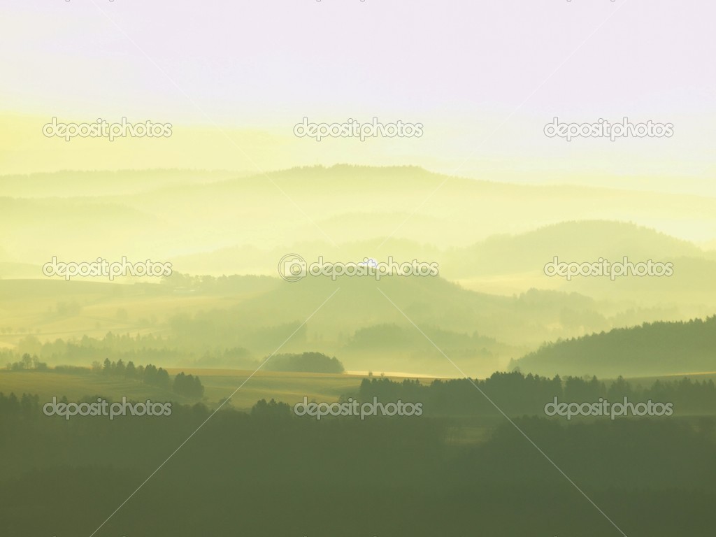 Golden autumn sunrise in a beautiful mountain of Bohemia. Peaks of hills increased from foggy background, the fog is yellow and orange due to sun rays.