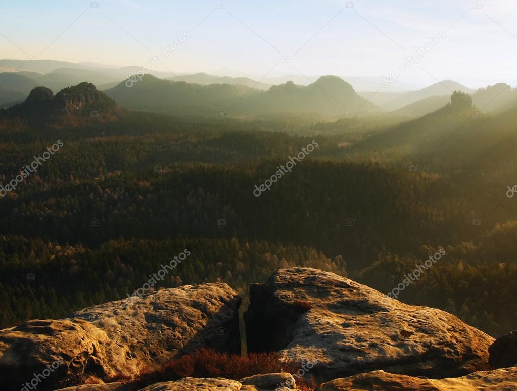 Cold spring sunrise between sandstone peaks increased from gentle mist, bright trails of sun rays in mist.