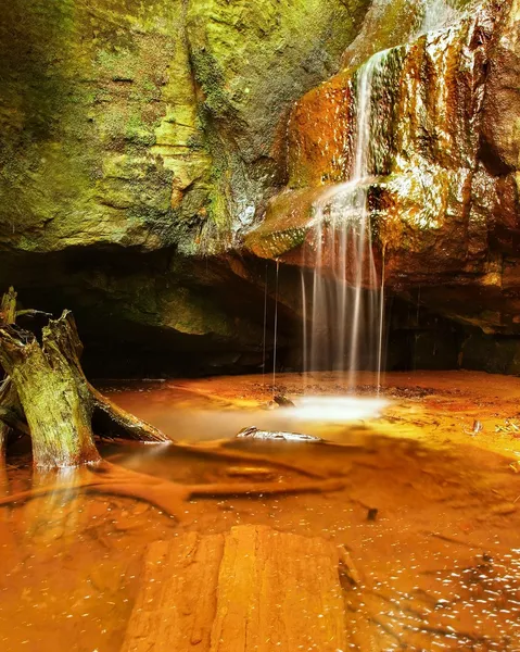 Kleiner Wasserfall auf kleinem Gebirgsbach, bemooster Sandsteinblock und Wasser springt in kleines Becken hinunter. Wasserströme mit Sonnenstrahlen, orangefarbener Sand mit Sedimenten darunter. — Stockfoto