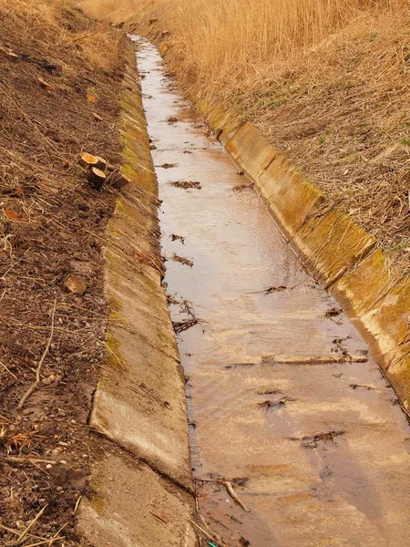 Im Frühjahr wurde der Entwässerungskanal zwischen den Wiesen gereinigt. Wasser im Abfluss, trockenes altes Gras am Ufer — Stockfoto