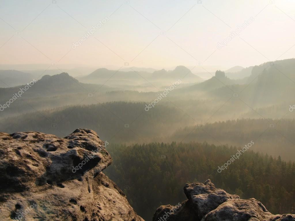 Spring sunrise in a beautiful mountain of Czech-Saxony Switzerland. Sandstone peaks increased from foggy background, bright trails of sun rays in mist.