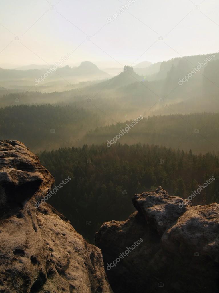 Spring sunrise in a beautiful mountain of Czech-Saxony Switzerland. Sandstone peaks increased from foggy background, bright trails of sun rays in mist.