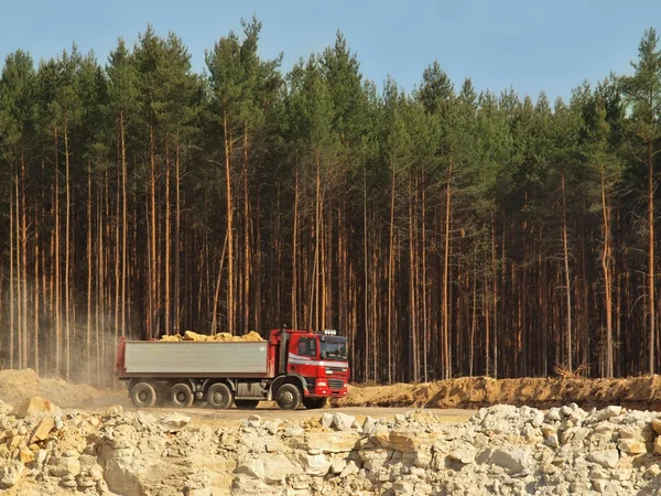 Grand camion avec cabine rouge et semi-remorque grise pleine de matériel chargé. Mine ouverte en forêt de pins — Photo