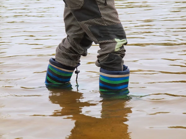 Jovem está lavando botas de borracha na água lamacenta da lagoa — Fotografia de Stock
