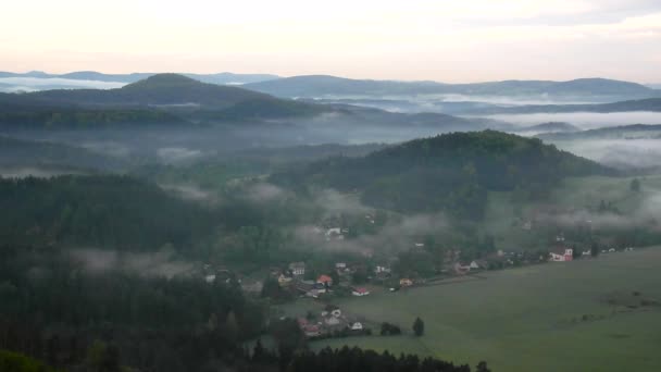 View into foggy vlley below view point in Bohemian Saxony Switzerland. The fog is moving between hills and peaks of trees and makes with sun rays gentle reflections. — Stock Video