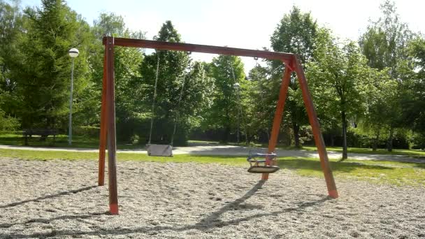 Auf dem Spielplatz schaukelt eine Kinderschaukel. sonniger Frühlingsmorgen, frische grüne Büsche und Bäume im Hintergrund. — Stockvideo