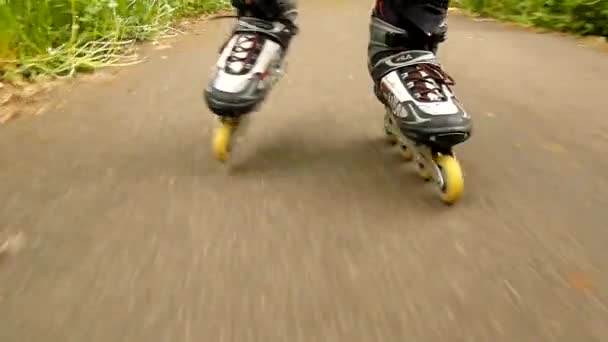 Una vista de cerca de las piernas en ropa deportiva con patines blancos rojos negros. El hombre está rápidamente patinando sobre asfalto camino en el parque, hierba y hojas en el suelo . — Vídeo de stock