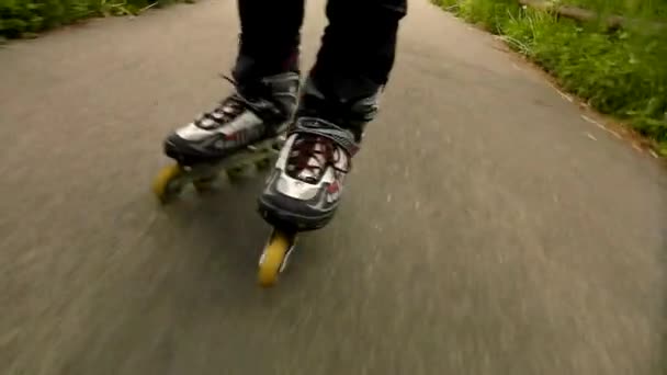 Una vista de cerca de las piernas en ropa deportiva con patines blancos rojos negros. El hombre está rápidamente patinando sobre asfalto camino en el parque, hierba y hojas en el suelo . — Vídeo de stock