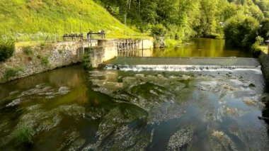 küçük bir nehrin akışı üzerinde küçük taşlı weir, soğuk su. küçük su çiçek blossom weir içinde dalgalanmalar çamurlu su altında. weir taşlı duvar