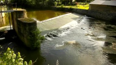 küçük bir nehrin akışı üzerinde küçük taşlı weir, soğuk su. küçük su çiçek blossom weir içinde dalgalanmalar çamurlu su altında. weir taşlı duvar