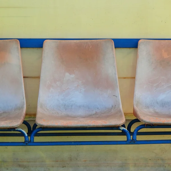 Old plastic seats on outdoor stadium players bench, chairs with worn paint below yellow roof. — Stock Photo, Image