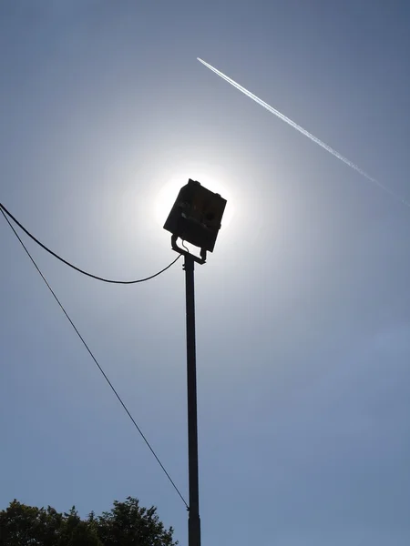 Hög utomhus lampost med pluged ledningar, planet flyger på himlen i bakgrunden. — Stockfoto