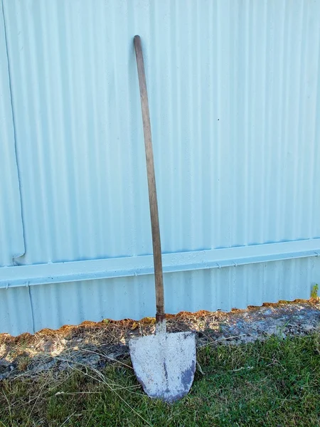 Old worn shovel lean on painted  metal sheet fence. Used handle of shovel. — Stock Photo, Image