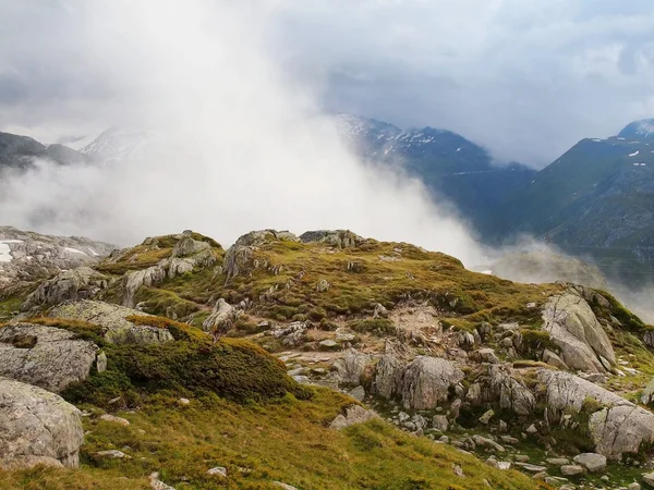 Sendero delgado en prados nevados de altas montañas alpinas por la noche. Picos oscuros en pesadas nubes brumosas. Fin frío y húmedo del día de primavera en las montañas de los Alpes . — Foto de Stock