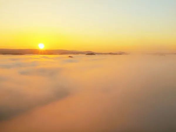 Deep misty valley in rocky park full of heavy clouds of dense fog. Sandstone peaks increased from foggy background, the Sun rays change its colors. — Stock Photo, Image