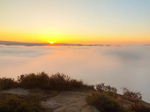 Autumn country. Deep misty valley full of morning heavy wisps of blue orange fog. Sandstone peaks increased from mist, dark hills and hot yellow Sun on horizon. — Stock Photo, Image