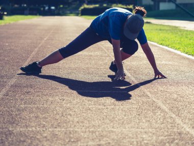Spor kadını bacak kaslarını esnetiyor ve okul stadında koşmadan önce geriye doğru eğiliyor.