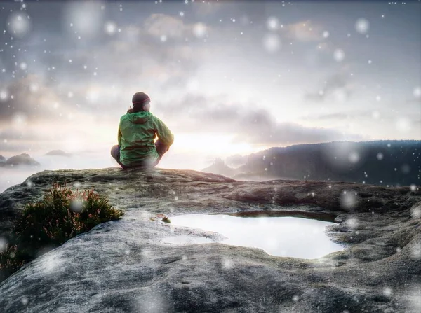 女徒步旅行者坐在山崖上 一边看日落 一边下雪 令人惊奇的秋天天气 空气中弥漫着薄雾和雪花 抽象照明 彩色照明弹 — 图库照片