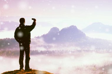 Kafanın üstünde tek bir telefon var ve puslu dağlarda selfie çekiyor. Vadide renkli sis var. Soyut aydınlatma, renkli işaret fişeği.