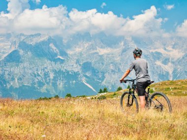 Gençler modern MTB 'de oturur ve tepeden tepeye taşlı ve karlı zirveleri seyrederler. Dolomite Alpleri, Trento bölgesi, İtalya 