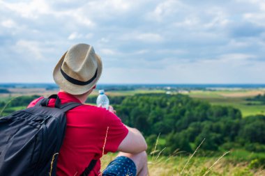 Gezgin dağlarda su içiyor. Sırt çantalı gezgin dağın tepesinde dinleniyor ve güneşli yaz gününde şişe su içiyor..