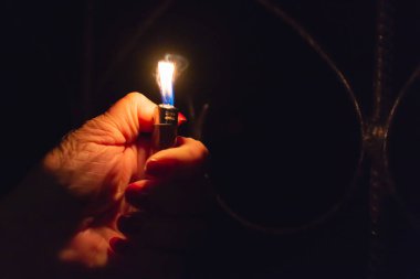 Karanlık arka planda yanan bir çakmak tutan bir kadın. Yaklaş, seçici odaklan. Boşluğu kopyala.