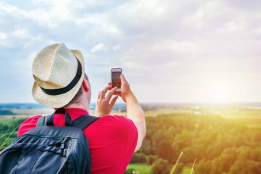 Sırt çantalı genç adam akıllı telefon kullanarak selfie çekiyor. Gökyüzü bulutlu yaz mevsimi aralığı. Manzara yaz arkaplanı. Aktif spor sırt çantalı sağlıklı yaşam tarzı konsepti..