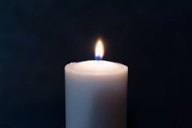 Siyah arkaplanda parlak bir mum yanıyor. Sarı mum alevi. Karanlıktaki mum alevi. Uzayı kopyala..