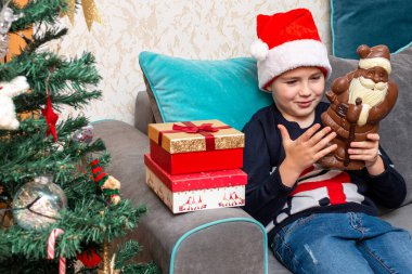 Kanepede oturan çocuk elinde Noel Baba çikolatalı hediyeler Noel Baba şapkalı çocuk..
