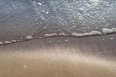 Kumlu akşam kumsalında denizin yumuşak dalgası. Odaklanma, bulanık görüntü. Boşluğu kopyala.