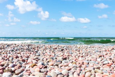 Kıyıda küçük çakıl taşları. Güneşli yaz günü mavi gökyüzü, beyaz bulutlar. Güzel, yalnız, küçük çakıl taşı plajı. Uzayı kopyala..