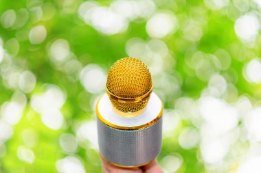 Karaoke için mikrofon tutan bulanık yeşil arka plandaki kadın el. Boşluğu kopyala.