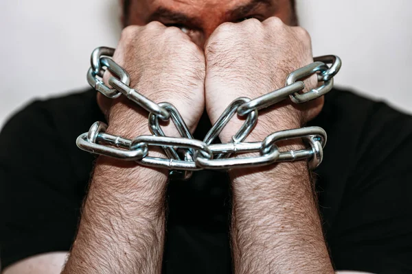 Angry man with chained hands.Two hands chained with an iron chain.Gray background,selective focus.Closeup.