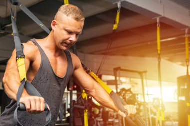 Spor salonunda egzersiz yapan kaslı bir adam, spor salonunda triseps egzersizi yapan. Güçlü çıplak erkek karın kası. Yakışıklı vücut geliştirici. Spor salonunda kapalı alanda çalışıyor..