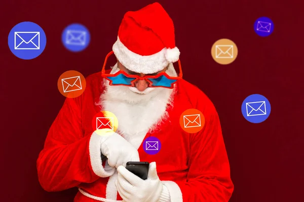 圣诞老人引起了社交媒体的注意 圣诞老人用他的电话收发电子邮件 红色工作室背景 — 图库照片