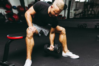 Genç sporcu spor salonunda biceps çalışıyor. Spor salonunda ağırlık kaldıran kaslı bir gencin yakın çekimi. Yakın plan.