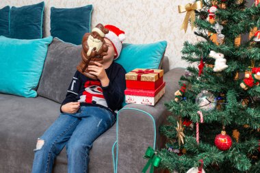 Kanepede oturan çocuk elinde Noel Baba çikolatalı hediyeler Noel Baba şapkalı çocuk..