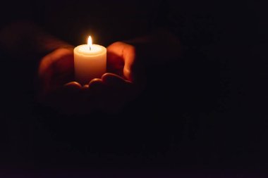 Eller karanlıkta yanan bir mum tutuyor. Seçmeli odak, siyah arkaplan. Uzayı kopyala..