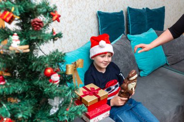 Kanepede oturan çocuk elinde Noel Baba çikolatalı hediyeler Noel Baba şapkalı çocuk..