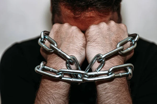 depressed man with chained hands.Two hands chained with an iron chain.Gray background,selective focus.Closeup.